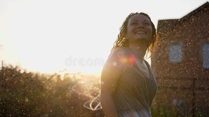 Una mujer sonriente feliz está bajo la lluvia. impresionantes rayos solares dorados brillan en una joven lúdica disfrutando de una almacen de metraje de vídeo