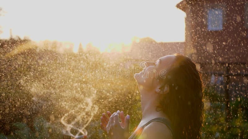 Una mujer sonriente feliz está bajo la lluvia. impresionantes rayos solares dorados brillan en una joven lúdica disfrutando de una almacen de video