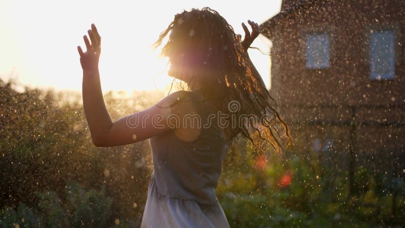 Una mujer sonriente feliz está bajo la lluvia. impresionantes rayos solares dorados brillan en una joven lúdica disfrutando de una metrajes