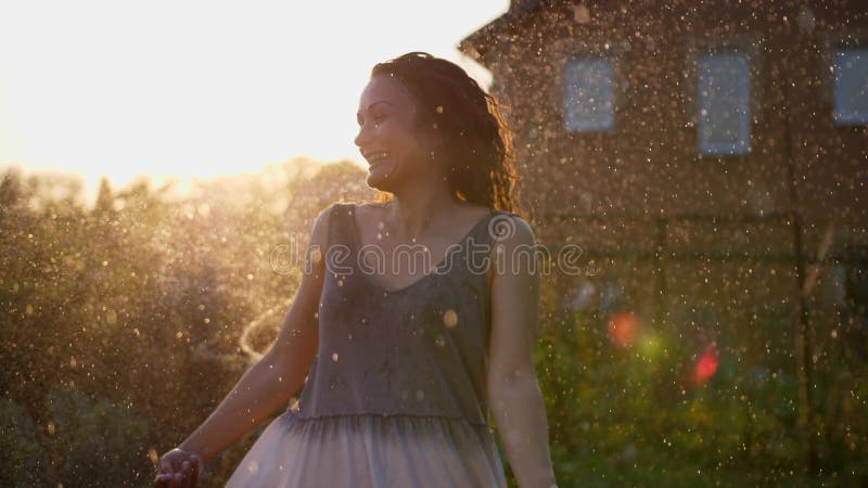 Una mujer sonriente feliz está bajo la lluvia. impresionantes rayos solares dorados brillan en una joven lúdica disfrutando de una metrajes
