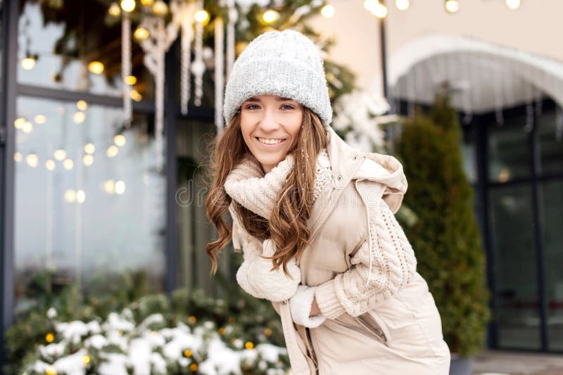 Una mujer sonriente se regocija en la ciudad con un sombrero y mitones en invierno fotos de archivo libres de regalías