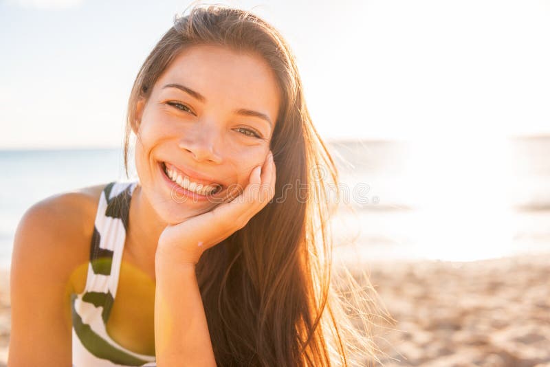 Una mujer sonrÃ­e feliz en la playa con una piel brillante saludable en el fondo de verano de los rayos solares. NiÃ±a asiÃ¡tica s