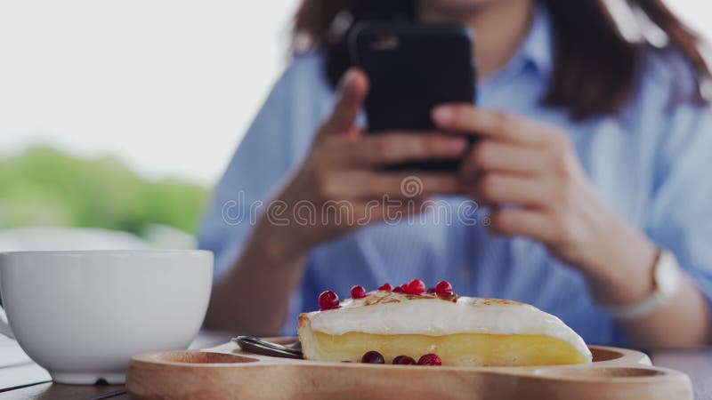 Una mujer usa un teléfono para tomar fotos de tarta de queso de fresa. una mujer tomando fotos promocionando comida en un café fav almacen de video