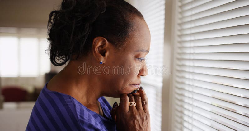 Una más vieja mujer negra triste mira hacia fuera su ventana imagen de archivo