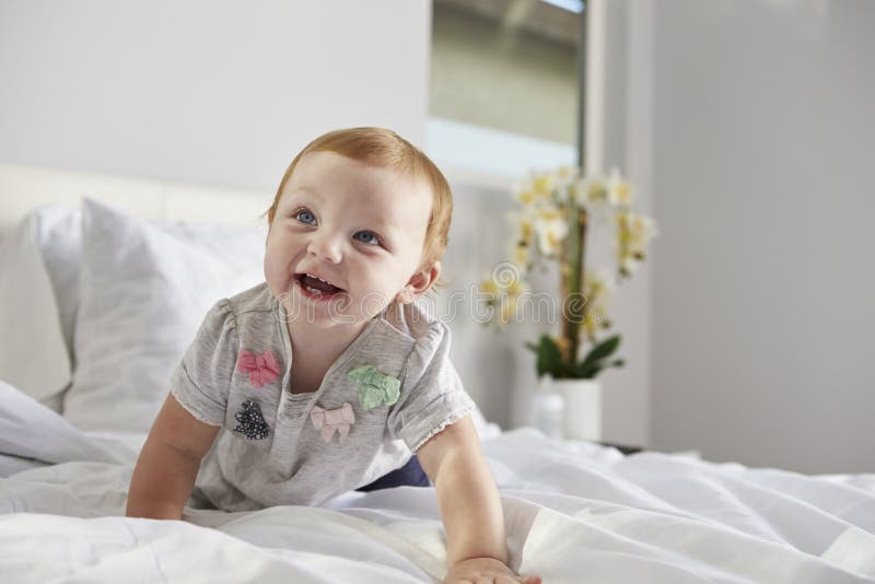 Una neonata felice che striscia su un letto, spazio della copia sulla destra immagine stock libera da diritti Una neonata felice che striscia su un letto, spazio della copia sulla destra immagine stock libera da diritti