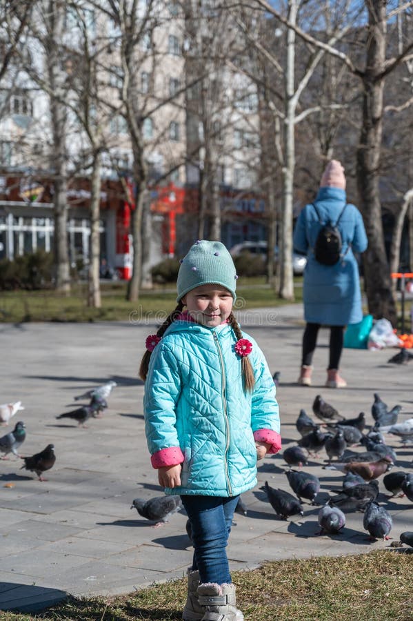 Una Niña Preescolar Con Una Chaqueta Azul Posa Afuera Frente a Una Bandada De De La Ciudad. Un Niño De Cinco Años Feliz Co Foto de archivo - Imagen de parque,
