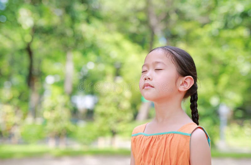 La niña asiática pacífica del niño cierra los ojos en el jardín con a respirar el aire fresco de la naturaleza. Retrato del niño r imagenes de archivo