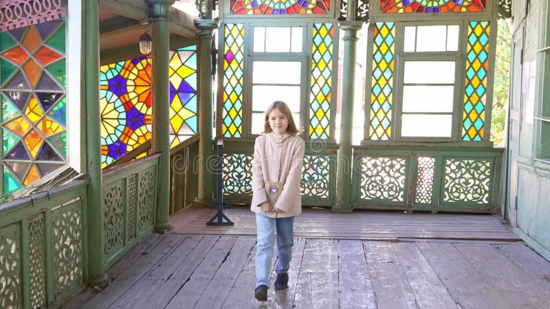 Una niña camina por la veranda con vidrieras multicolores.