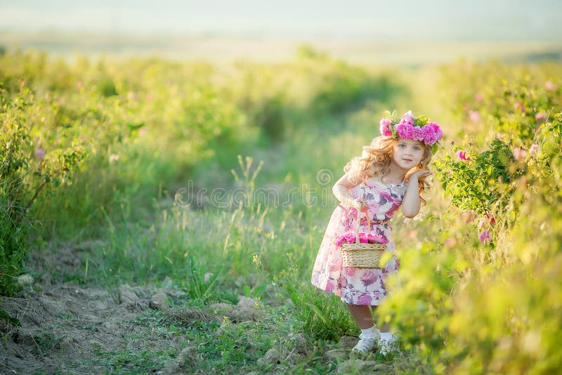 Una niña con el pelo rubio largo hermoso, vestido en un vestido ligero y una guirnalda de flores reales en su cabeza, en fotografía de archivo Una niña con el pelo rubio largo hermoso, vestido en un vestido ligero y una guirnalda de flores reales en su cabeza, en fotografía de archivo