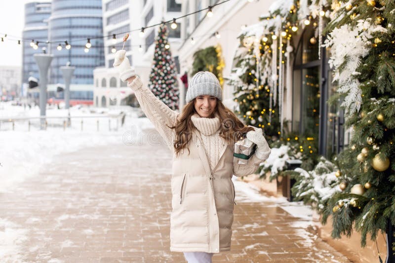 Una niña feliz camina por la ciudad en la nieve con un colorido chupete redondo y una caja de regalo fotografía de archivo libre de regalías