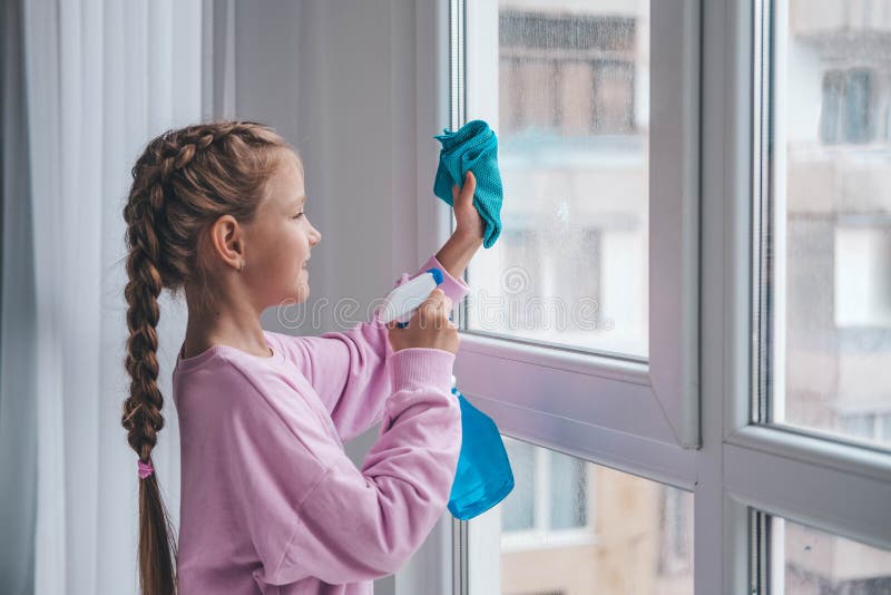 A little girl in a purple sweater sprinkles water from a bottle on the window and wipes it off with a rag. The child helps with cleaning the house. Clean the window. A little girl in a purple sweater sprinkles water from a bottle on the window and wipes it off with a rag. The child helps with cleaning the house. Clean the window