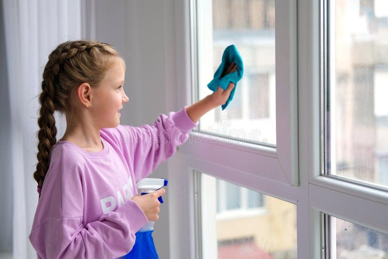 A little girl in a purple sweater sprinkles water from a bottle on the window and wipes it off with a rag. The child helps with cleaning the house. Clean the window. A little girl in a purple sweater sprinkles water from a bottle on the window and wipes it off with a rag. The child helps with cleaning the house. Clean the window