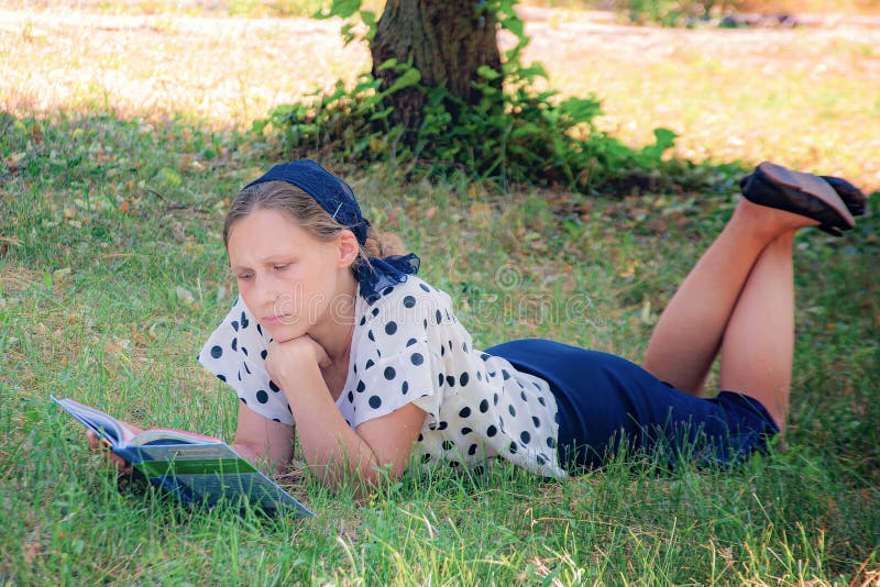 A girl lies on the grass under a tree and reads a book. A girl lies on the grass under a tree and reads a book.