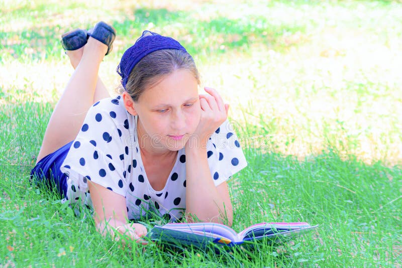 A girl lies on the grass under a tree and reads a book. A girl lies on the grass under a tree and reads a book.