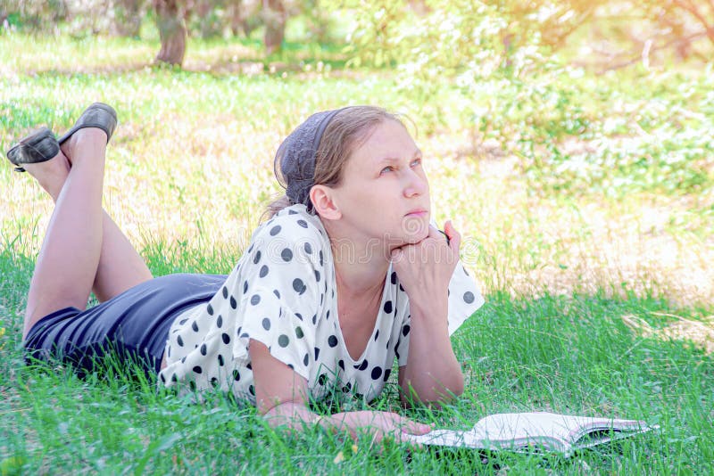 A girl lies on the grass under a tree and reads a book. A girl lies on the grass under a tree and reads a book.