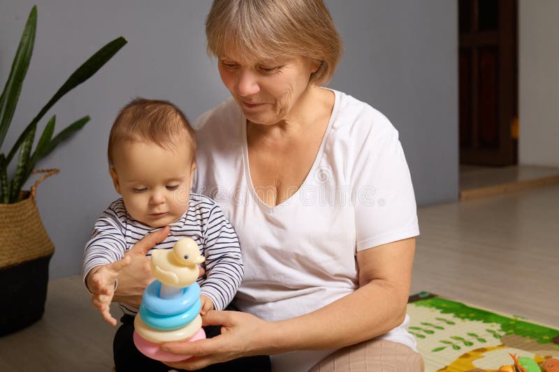 Una nonna e il suo bambino seduti sul pavimento, impegnati in un'interazione giocosa con un giocattolo impilante e colorato.. cond immagine stock libera da diritti