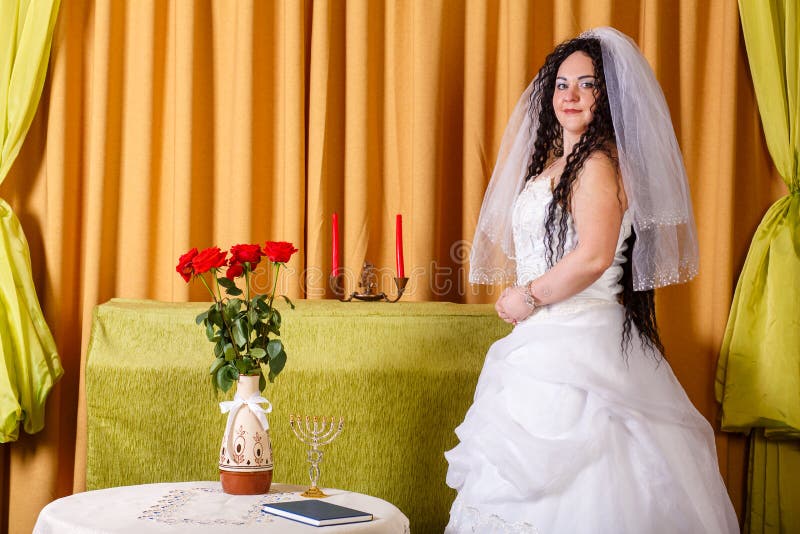 Una Novia Judía Con Un Vestido De Novia Blanco Con Velo Se Para En El Pasillo En Una Mesa Con Flores Y Reza Ante El Imagen de archivo - Imagen de rasgones, Una Novia Judía Con Un Vestido De Novia Blanco Con Velo Se Para En El Pasillo En Una Mesa Con Flores Y Reza Ante El Imagen de archivo - Imagen de rasgones,
