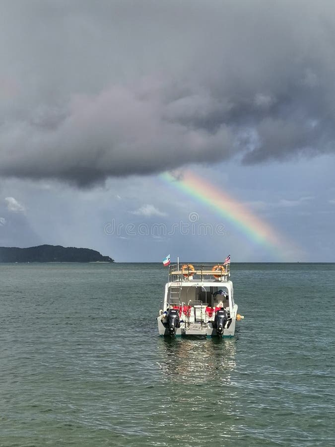 Una nuvola scura con un bellissimo arcobaleno che brilla molto lontano prima di partire per un'immersione ricreativa a Tunku Abdu immagine stock Una nuvola scura con un bellissimo arcobaleno che brilla molto lontano prima di partire per un'immersione ricreativa a Tunku Abdu immagine stock