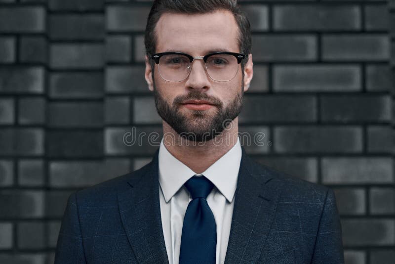 Una opinión confiada el líder Un hombre de negocios joven en vidrios y con una barba mira directamente usted fotos de archivo Una opinión confiada el líder Un hombre de negocios joven en vidrios y con una barba mira directamente usted fotos de archivo