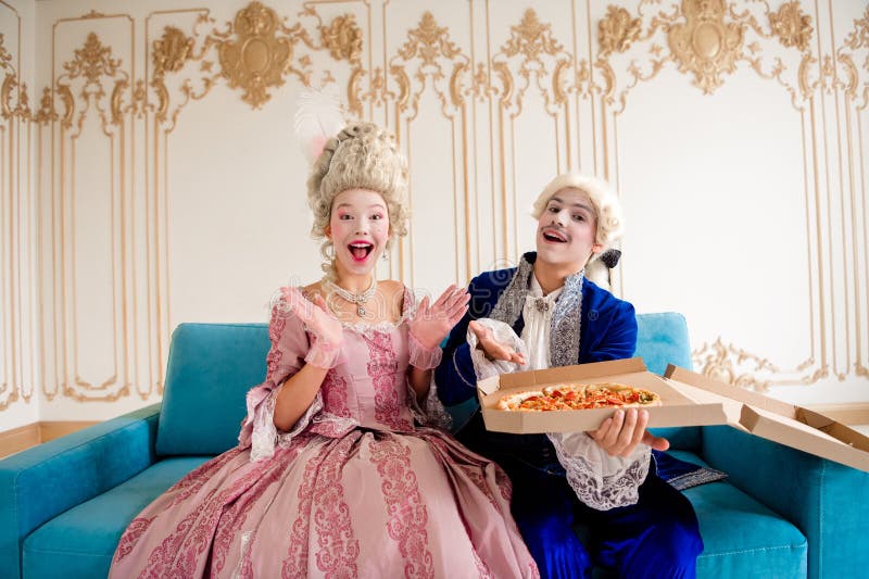Una pareja aristocrática vestida con un traje barroco puede disfrutar de una pizza en un salón de estilo retro con un ambiente aco imagenes de archivo