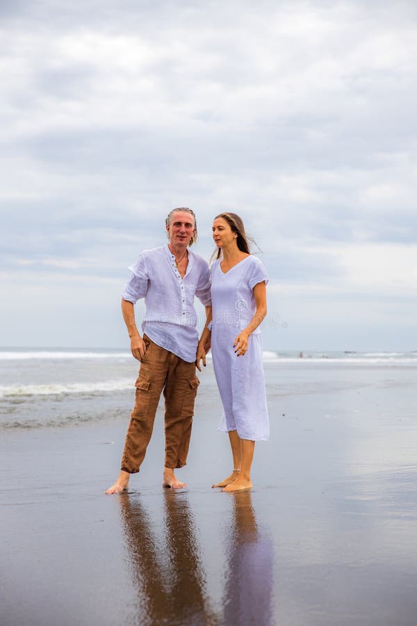 Una Pareja Caminando Descalzo La Playa. Hombre Con Pantalones Marrones Y Camisa Blanca. Mujer Vestida De Blanco. Y Muje Foto de archivo - de asia, amor: 205321434