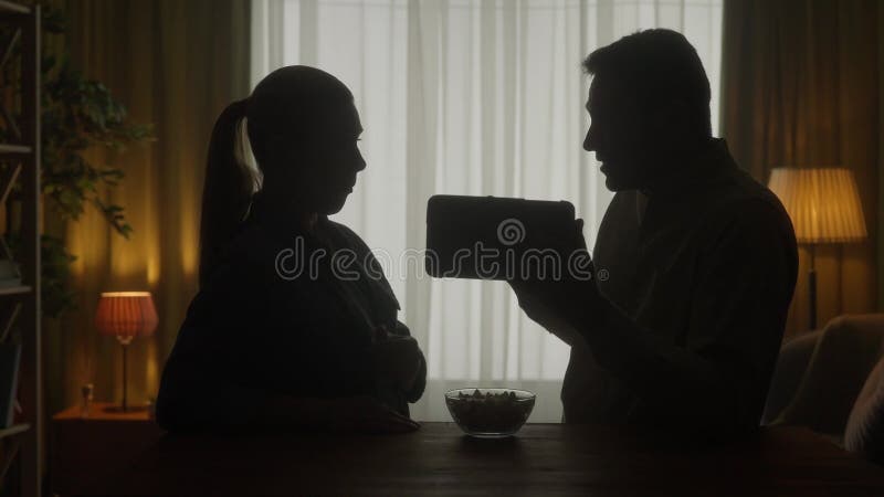 Una pareja está de pie en la mesa viendo una película de video en una tableta. discuten lo que vieron comer palomitas de maíz. la metrajes
