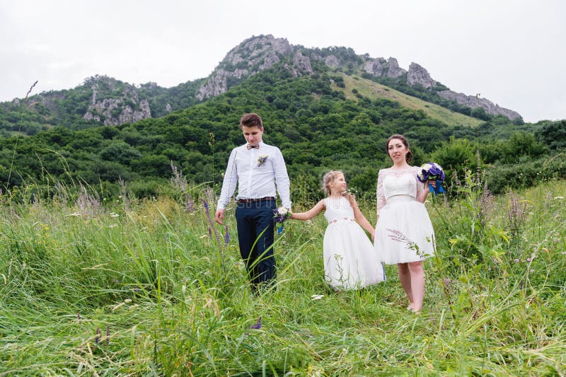Una pareja joven y su hija en vestidos de boda están caminando en naturaleza imagenes de archivo