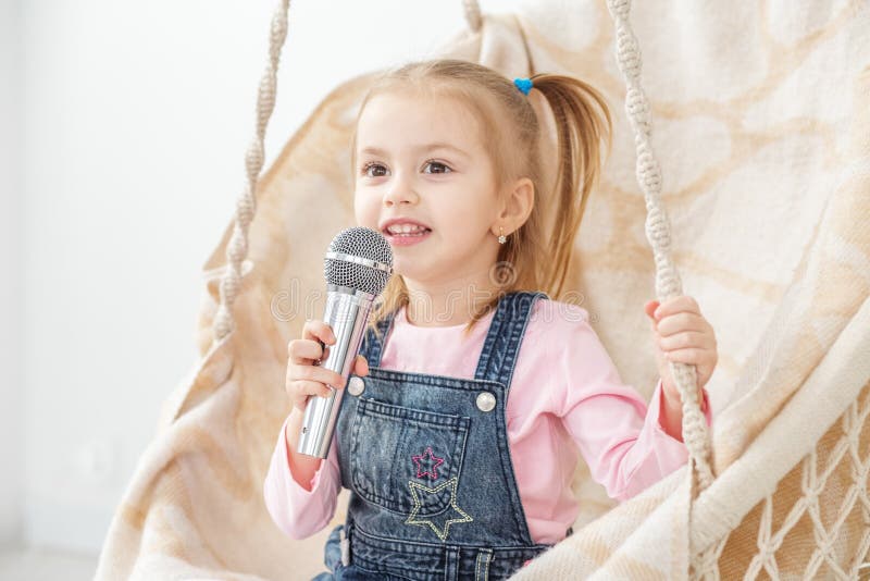 Una pequeña muchacha alegre canta una canción en el micrófono La estafa fotografía de archivo libre de regalías Una pequeña muchacha alegre canta una canción en el micrófono La estafa fotografía de archivo libre de regalías