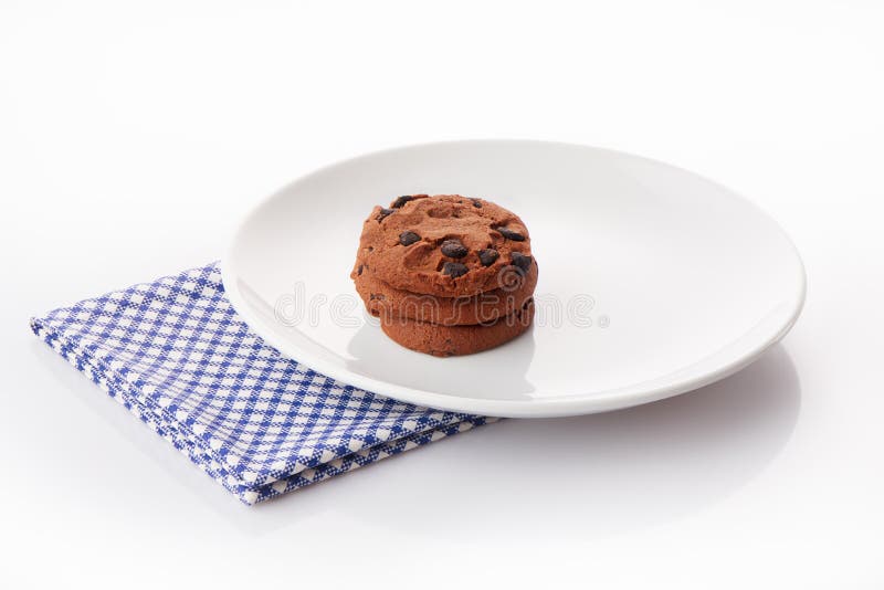 Una pila di tre biscotti di pepita di cioccolato casalinghi sul piatto ceramico bianco sul tovagliolo blu fotografie stock libere da diritti Una pila di tre biscotti di pepita di cioccolato casalinghi sul piatto ceramico bianco sul tovagliolo blu fotografie stock libere da diritti