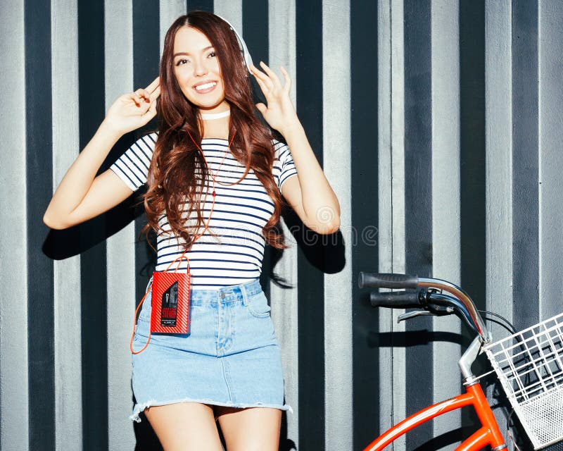 Una ragazza asiatica incredibilmente bella in un'attrezzatura dell'estate gode della musica Cuffie e giranastri d'annata rosso immagine stock Una ragazza asiatica incredibilmente bella in un'attrezzatura dell'estate gode della musica Cuffie e giranastri d'annata rosso immagine stock