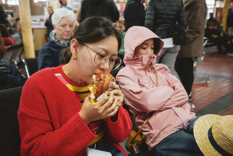 Una ragazza asiatica sta mangiando Amburgo per la prima colazione in Maria Reiche Neuman Airport nel Perù Lei ed il suo amico gua