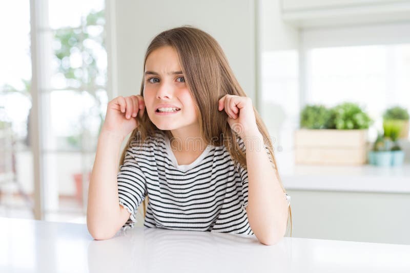 Una ragazza bellissima, con una camicia a strisce che copre le orecchie con le dita con un'espressione irritata per il rumore dell fotografia stock libera da diritti
