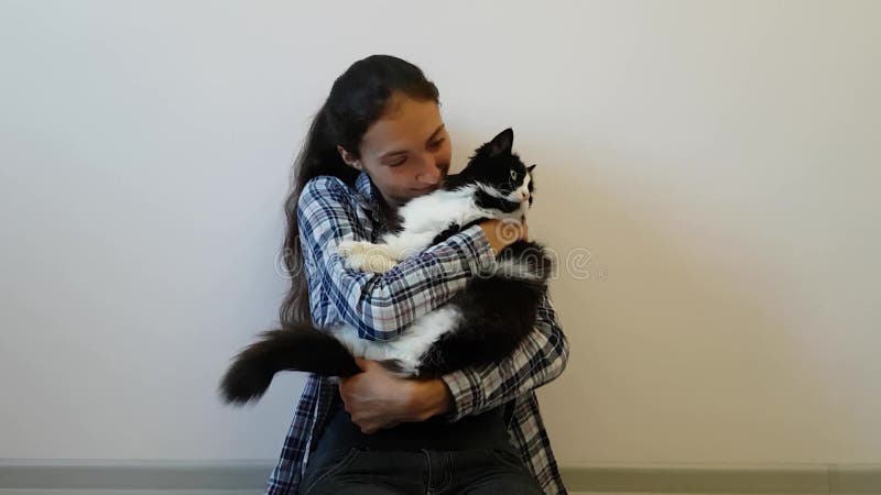 Una ragazza in una camicia di plaid abbraccia il suo gatto in bianco e nero favorito Il gattino paffuto non è molto soddisfatto d