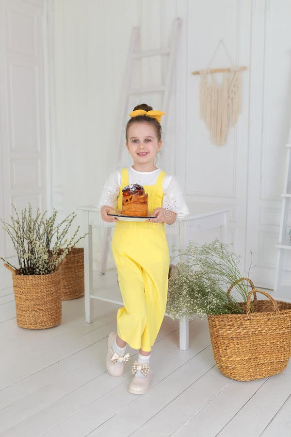 Una ragazza carina in tute gialle con la torta pasquale in mano. Sorridete bambini che tengono una torta di Pasqua per festeggiare fotografia stock libera da diritti