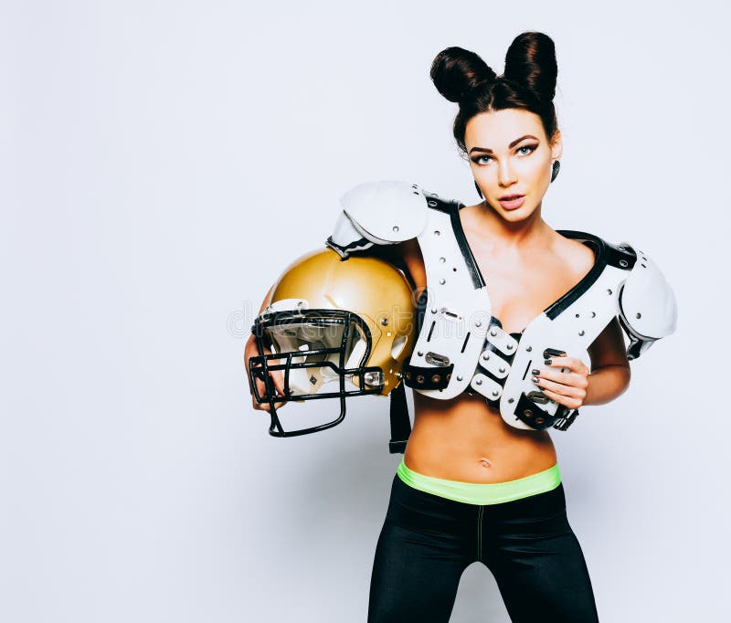 Una ragazza castana incredibilmente bella e atletica in shoulderpads e un casco di football americano che dimostra stordimento fotografia stock Una ragazza castana incredibilmente bella e atletica in shoulderpads e un casco di football americano che dimostra stordimento fotografia stock