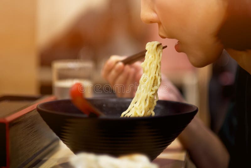 Una ragazza che mangia le tagliatelle giapponesi in ristorante giapponese immagine stock libera da diritti Una ragazza che mangia le tagliatelle giapponesi in ristorante giapponese immagine stock libera da diritti