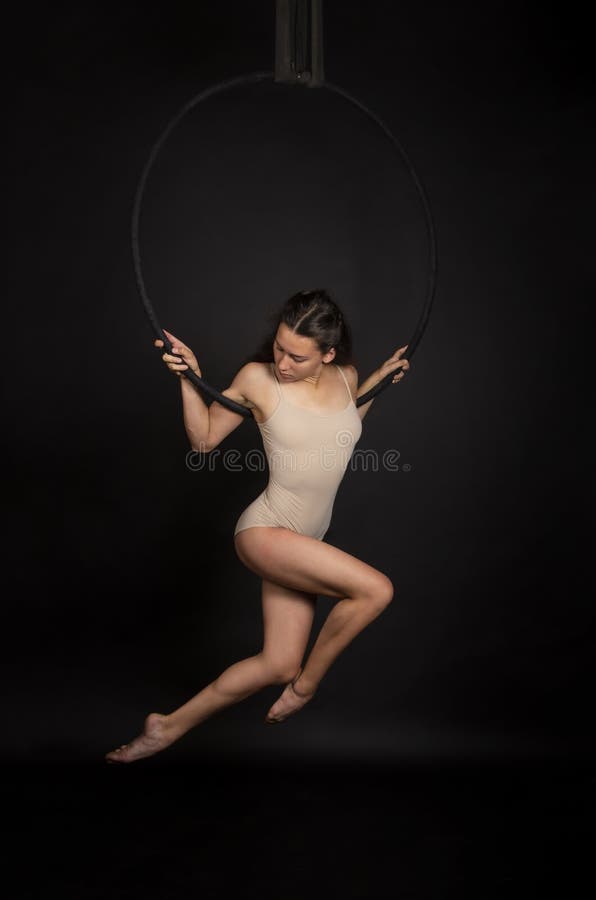 Una ragazza con i capelli lunghi è impegnata in acrobazie aerea in una tuta beige si esercita nell'anello dell'aria fotografia stock libera da diritti