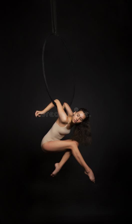 Una ragazza con i capelli lunghi è impegnata in acrobazie aerea in una tuta beige si esercita nell'anello dell'aria immagine stock libera da diritti