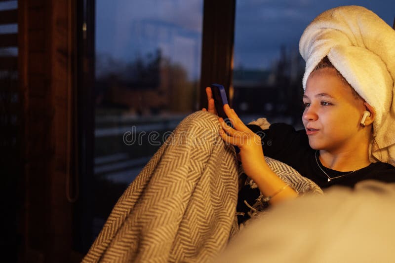 Una ragazza con un asciugamano in testa guarda lo schermo del telefono e sorride. Un ragazzo carino sta tenendo un cellulare e chi fotografie stock