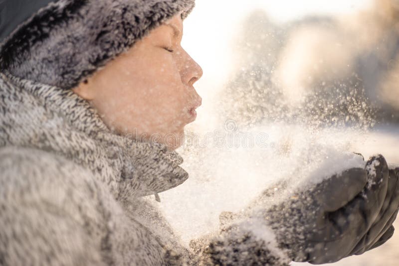 Una ragazza di bellezza che soffia sulla neve sui precedenti di inverno immagine stock Una ragazza di bellezza che soffia sulla neve sui precedenti di inverno immagine stock