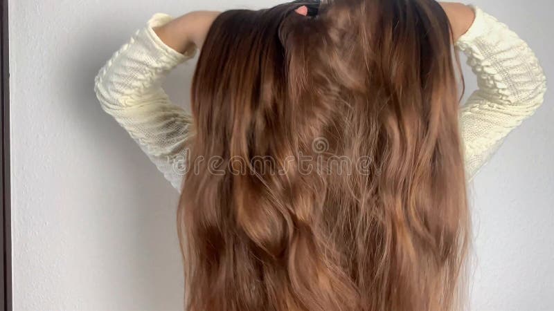Una ragazza europea in abito bianco pettina i suoi capelli lunghi naturali in casa, raddrizza il concetto di acconciatura