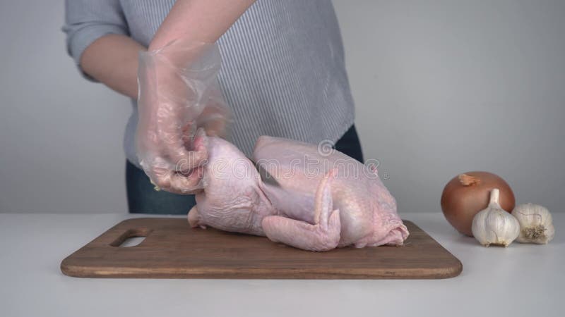 Una ragazza in guanti è impegnata a tagliare una carcassa di pollo