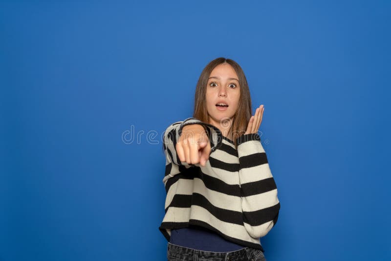 Una ragazza ispanica eccitata e positiva di circa 15 anni con un maglione a strisce che ti punta il dito indice contro e fotografie stock