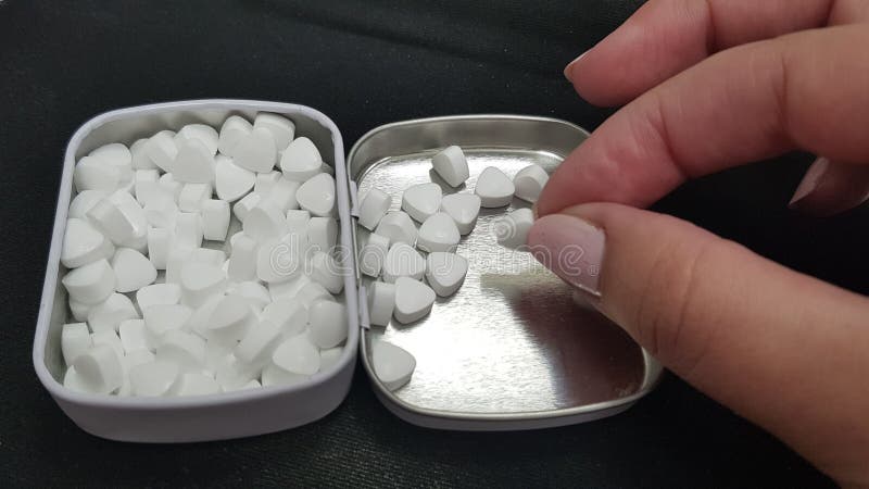 Una ragazza prende una piccola caramella bianca dalla copertura del contenitore aperto di metallo fotografia stock Una ragazza prende una piccola caramella bianca dalla copertura del contenitore aperto di metallo fotografia stock