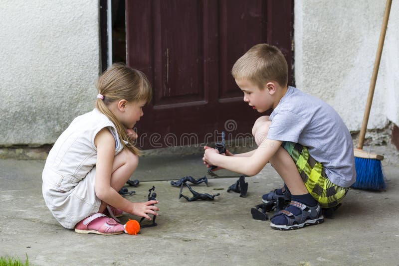 Una ragazza prescolare graziosa bionda di due bambini svegli e ragazzo bello che giocano all'aperto con i giocattoli di plastica fotografie stock Una ragazza prescolare graziosa bionda di due bambini svegli e ragazzo bello che giocano all'aperto con i giocattoli di plastica fotografie stock