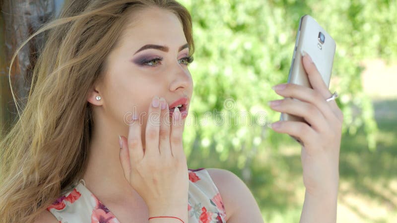 Una ragazza regola il suo trucco con un telefono fotografie stock Una ragazza regola il suo trucco con un telefono fotografie stock