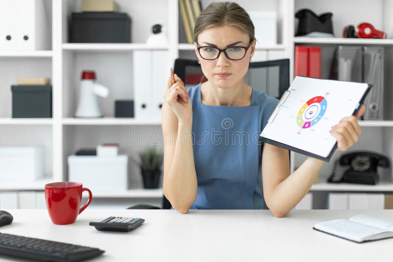 Una ragazza si siede ad una tavola nell'ufficio e tiene una penna e un documento con un diagramma fotografia stock libera da diritti