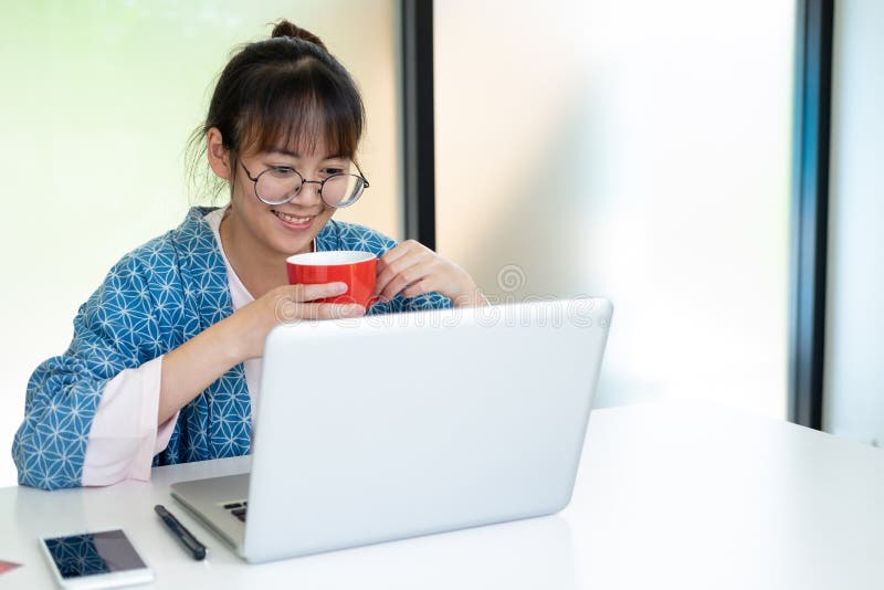 Una ragazza sorridente mentre regge la tazza di caffè e guarda lo schermo del portatile immagini stock libere da diritti Una ragazza sorridente mentre regge la tazza di caffè e guarda lo schermo del portatile immagini stock libere da diritti