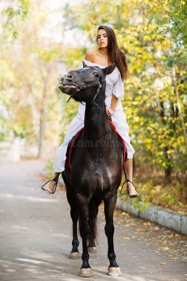 Una ragazza sta guidando su un cavallo nero che la esamina all'esterno fotografie stock Una ragazza sta guidando su un cavallo nero che la esamina all'esterno fotografie stock