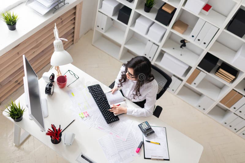 Una ragazza sta lavorando al computer nell'ufficio e tiene una penna e un taccuino in sua mano immagini stock libere da diritti
